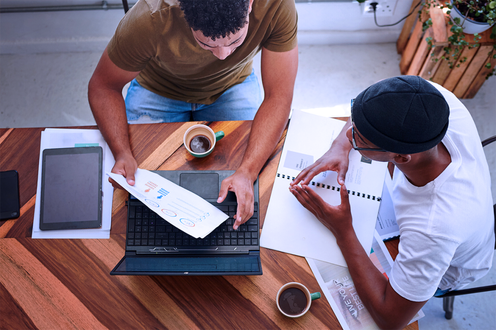 Mid Size Business Owners Drinking Coffee and Discussing Marketing Challenges at a Table Crunching Numbers