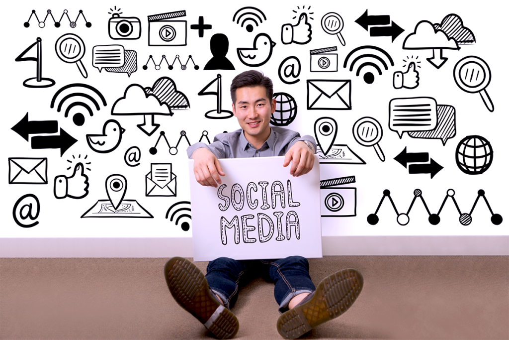 Small Business Owner Sitting In Front of a Social Media Icon Wall Holding a Sign