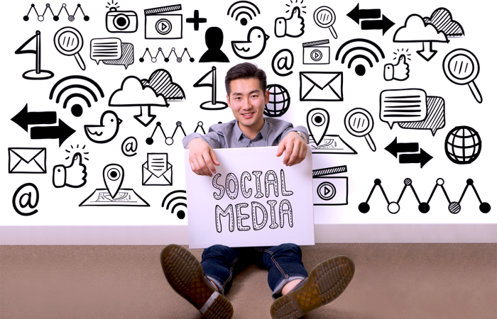 Small Business Owner Sitting In Front of a Social Media Icon Wall Holding a Sign